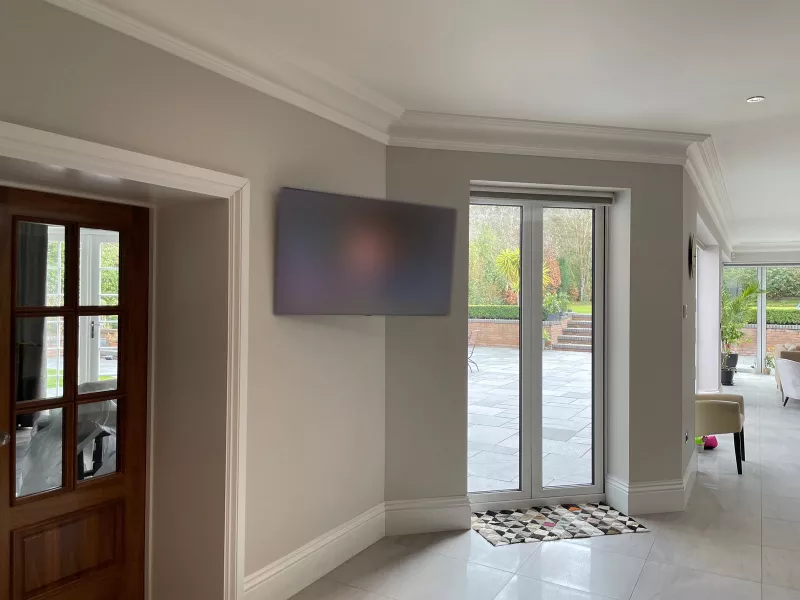 A wall mounted TV next to glazed doors that open onto a paved terrace