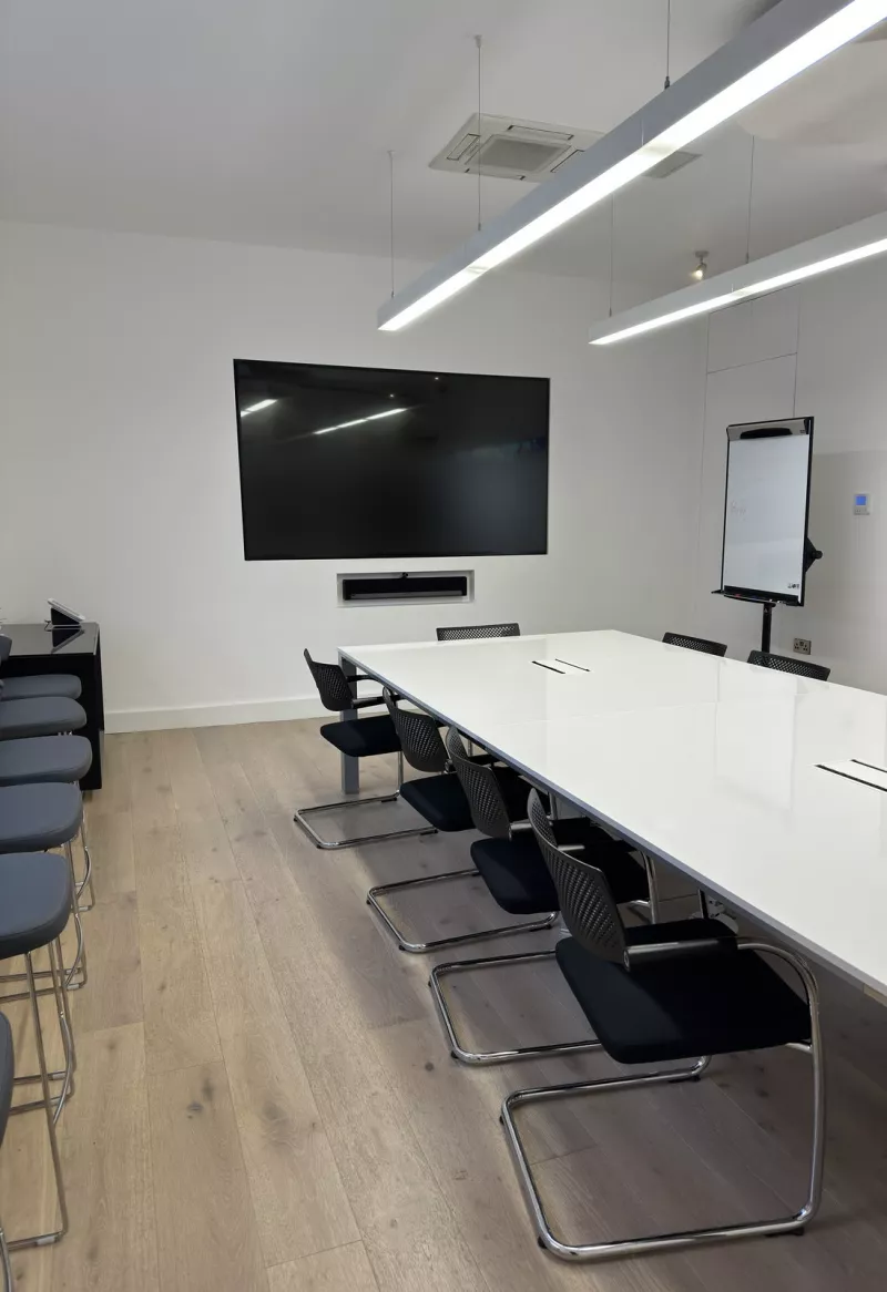 A second view of the meeting room from the side, showing the wall display, the recessed soundbar, the flip chart and the long white table