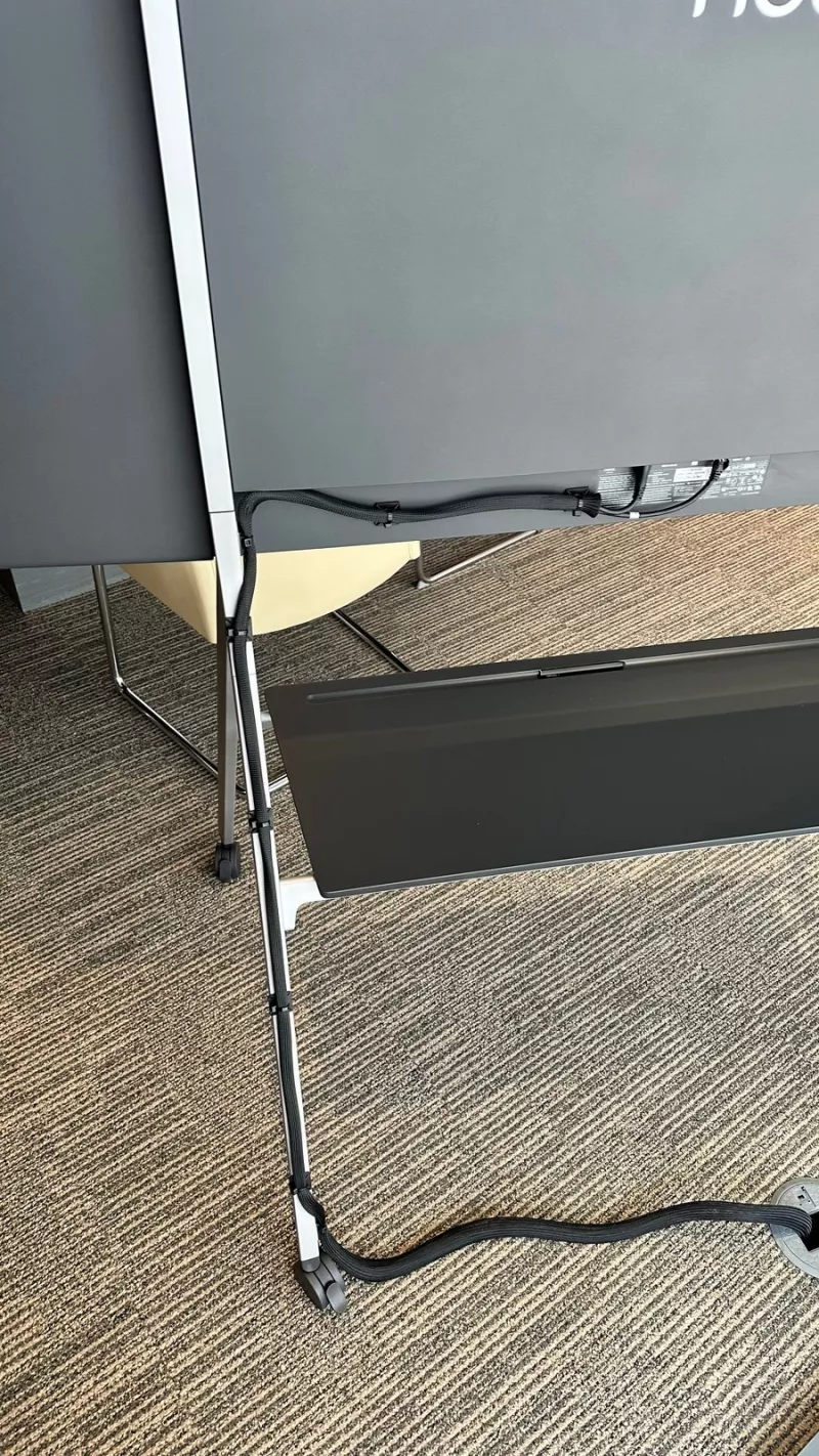Black cable sleeve running down the rear leg of the Neat Board stand to the floor