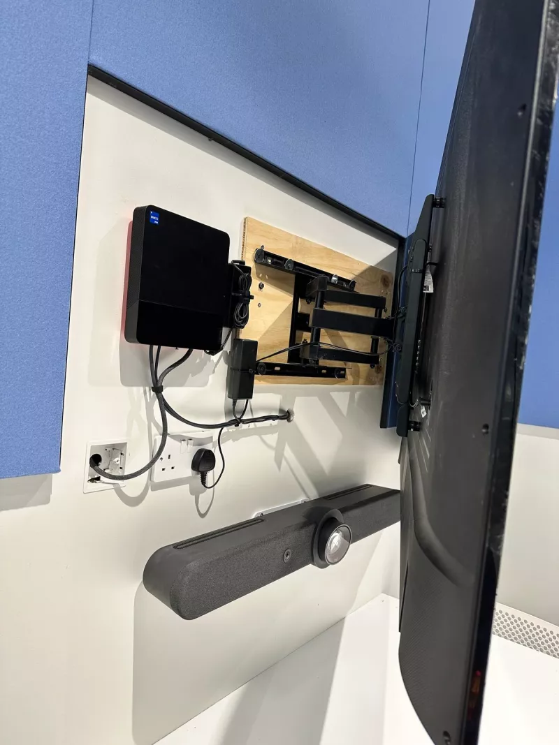 The display swung out from the wall on its arm, fixed to a timber backing board, with a small black unit beside it and the video bar below