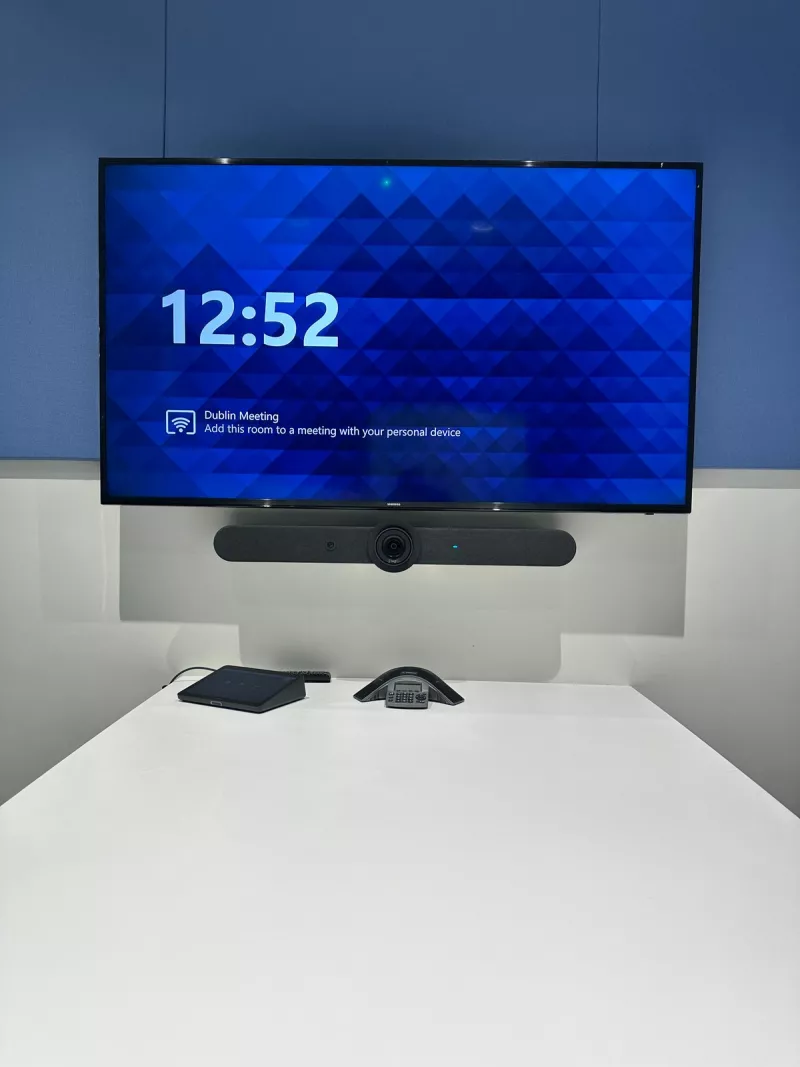 Samsung display with a Logitech video bar fixed below it, and a Logitech Tap touch controller and a speakerphone on the white table