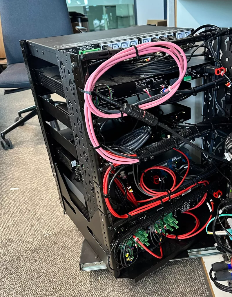 Rear of the AV rack with pink cables looped and tied back, red cables running to green screw terminals and power outlets along the top
