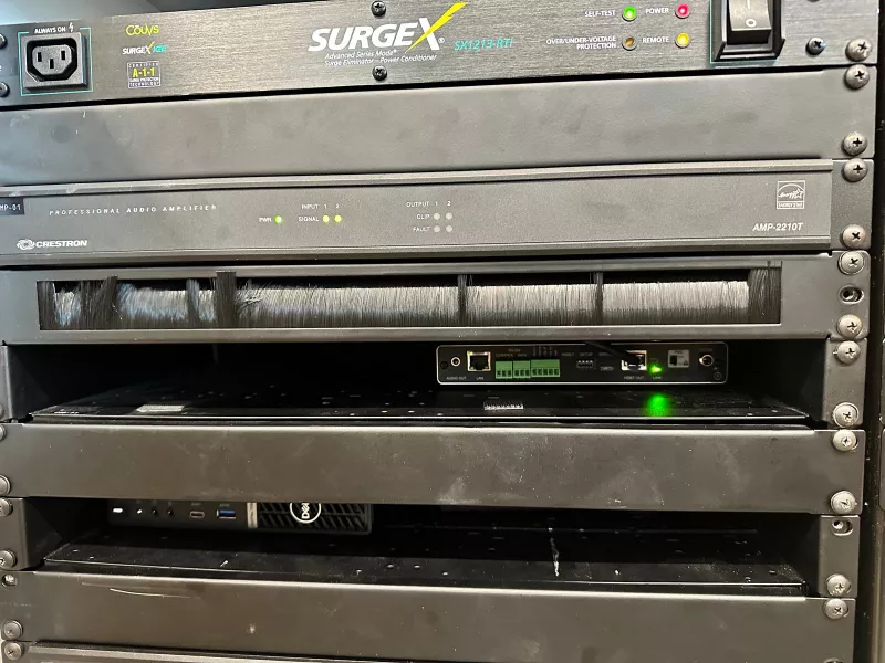 Front of the AV rack with a SurgeX power conditioner, a Crestron amplifier, a cable brush panel and a Dell mini PC on its own shelf