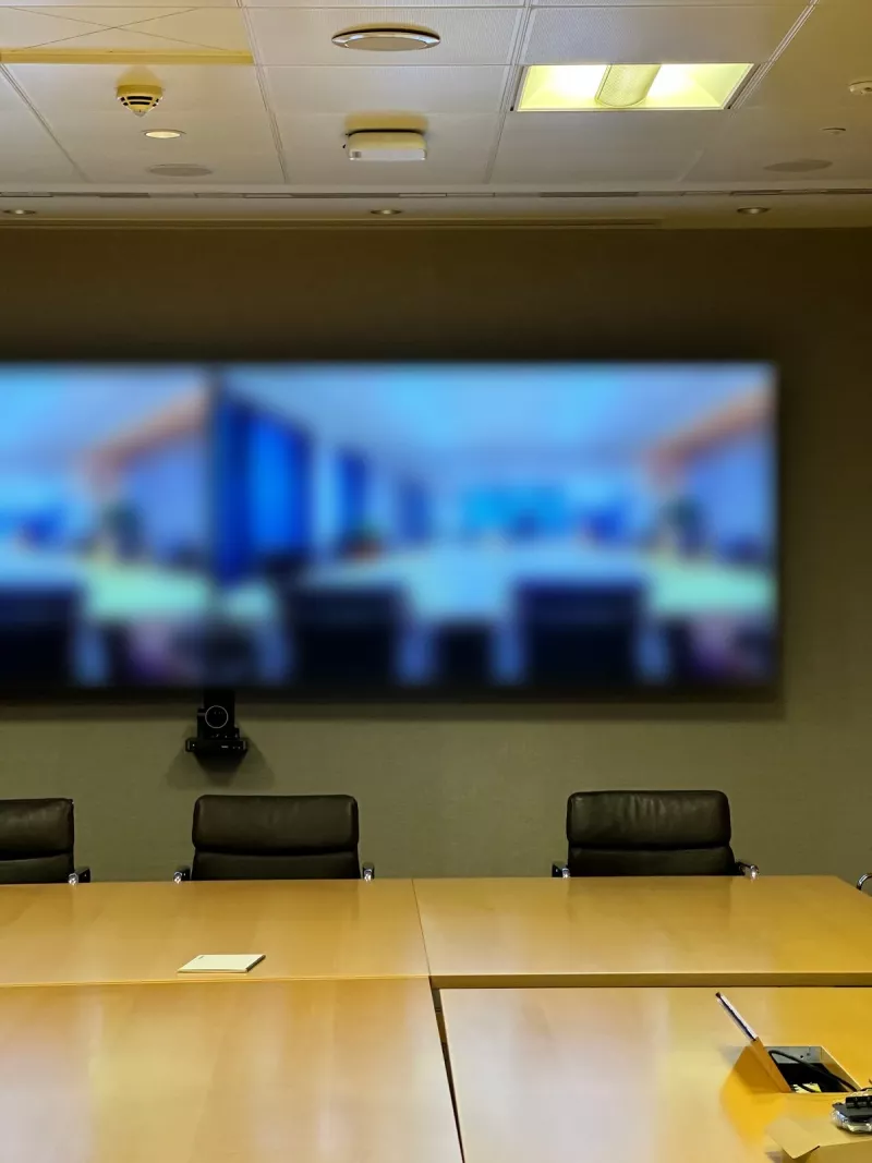 A straight on view of the two screens and the camera mounted below them, with black leather chairs along the end of the table