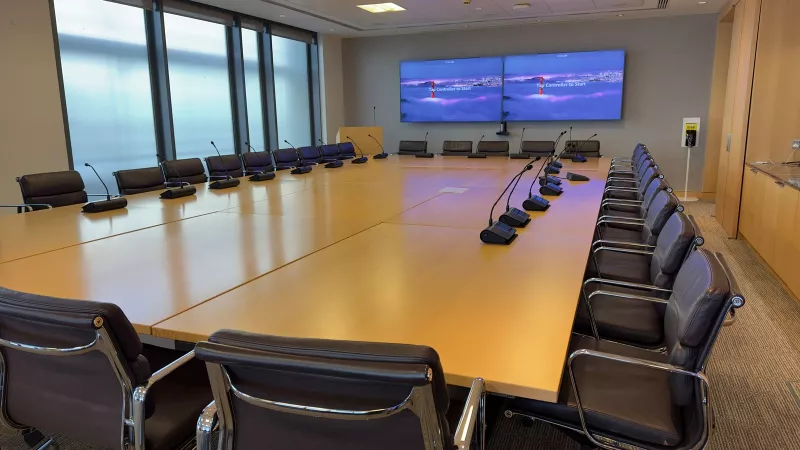 Boardroom audio system in Dublin city centre, with conference microphones along both sides of the timber table and Zoom Rooms on the twin screens at the far end