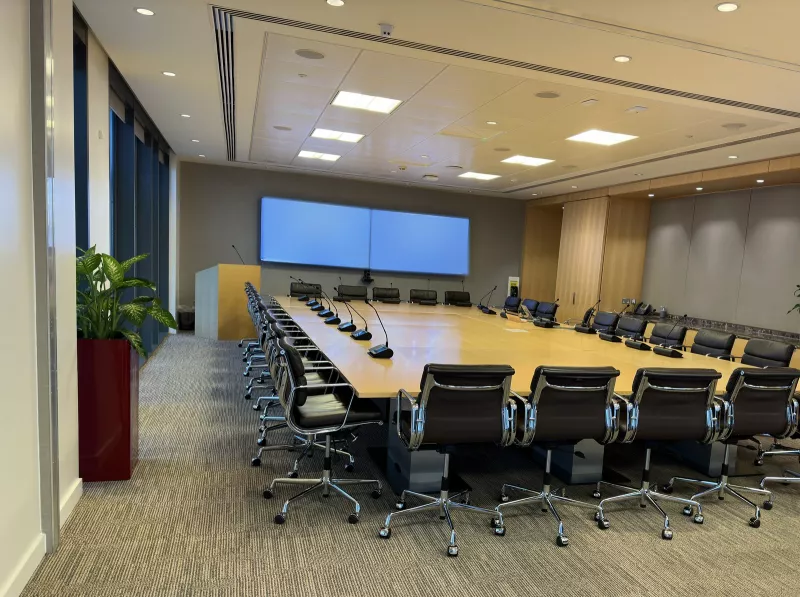 The boardroom seen from the door: black leather chairs around a very large timber table, a lectern with its own microphone and twin screens on the far wall