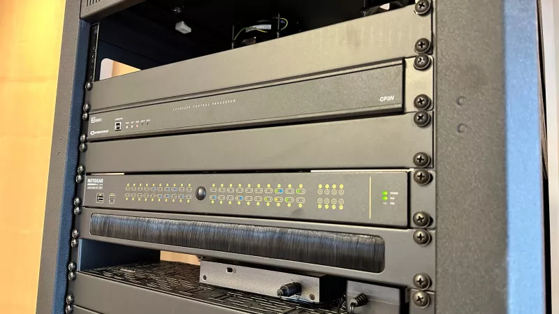 A Crestron CP3N control processor above a Netgear AV Line network switch, with a brush panel below it for the cables