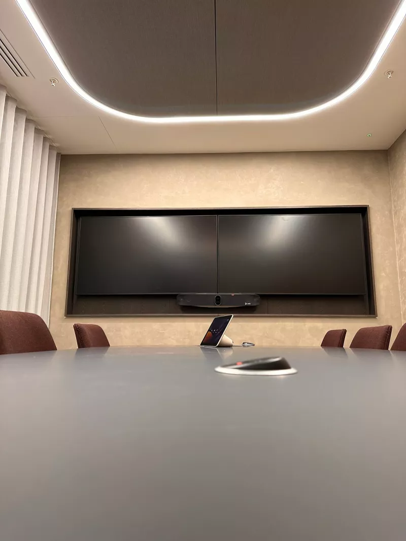 A Poly video bar below two displays set side by side in a wall recess, with a touch controller on the meeting table