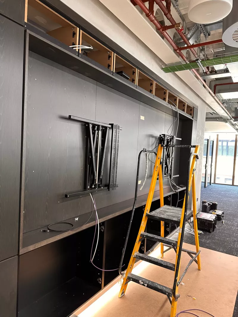 A pair of display arms fixed into a dark joinery unit before the screens arrived, cables ready alongside