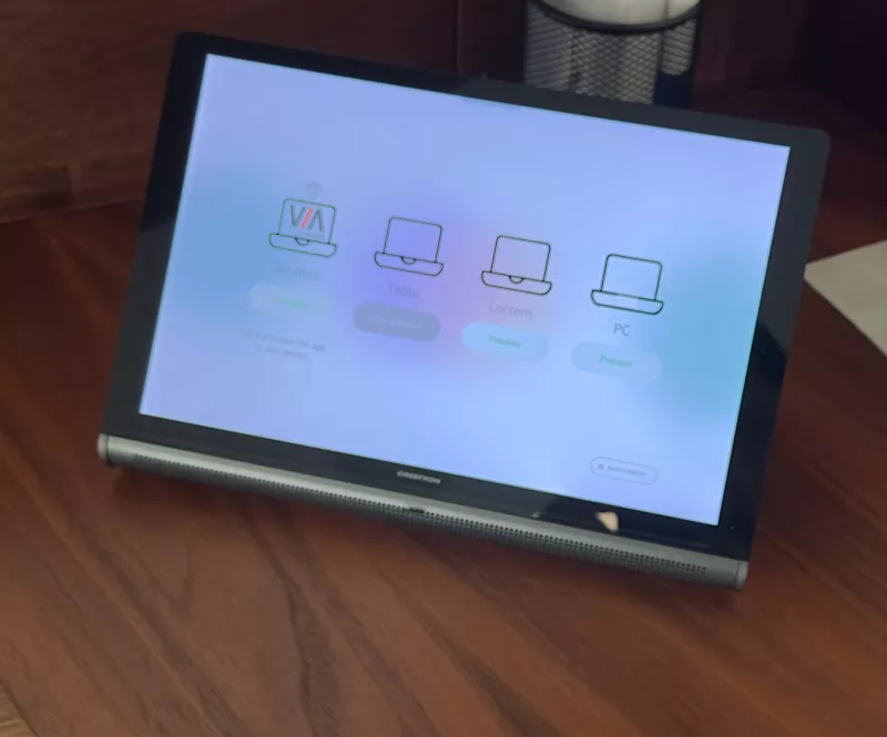 A Crestron touch panel on a dark timber desk offering four sources: wireless through Kramer VIA, the table, the lectern and a PC