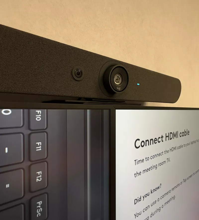 Close up of the Logitech video bar above the join between the two screens, which show the guide to connecting a laptop