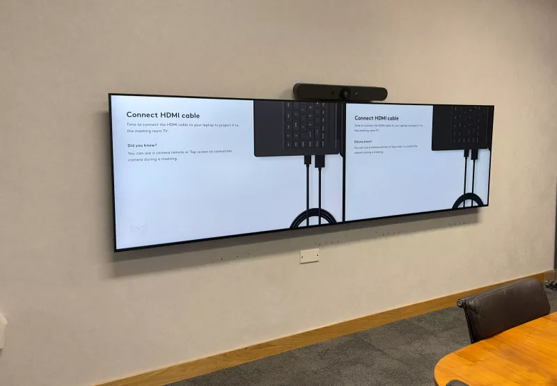 Meeting room technology in a Dublin city centre office: twin screens side by side with a Logitech video bar above them, beside an oval timber table