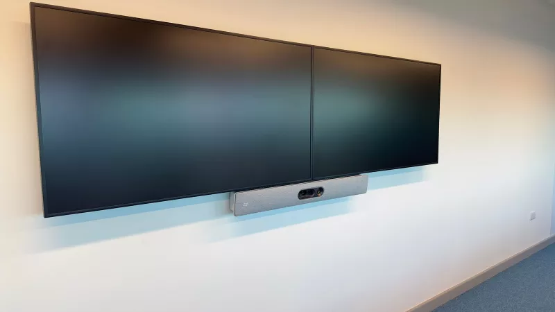 Twin screens on a white wall with a grey Cisco video bar mounted below the join