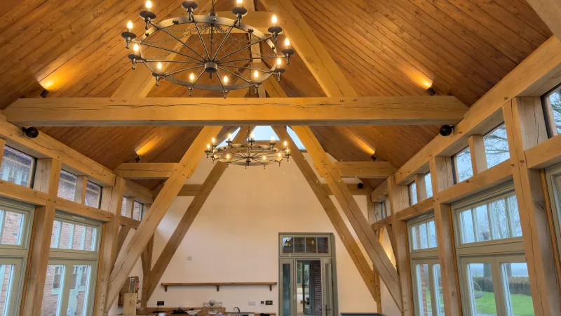 The finished oak frame room under a vaulted pine ceiling, lit by two wheel chandeliers