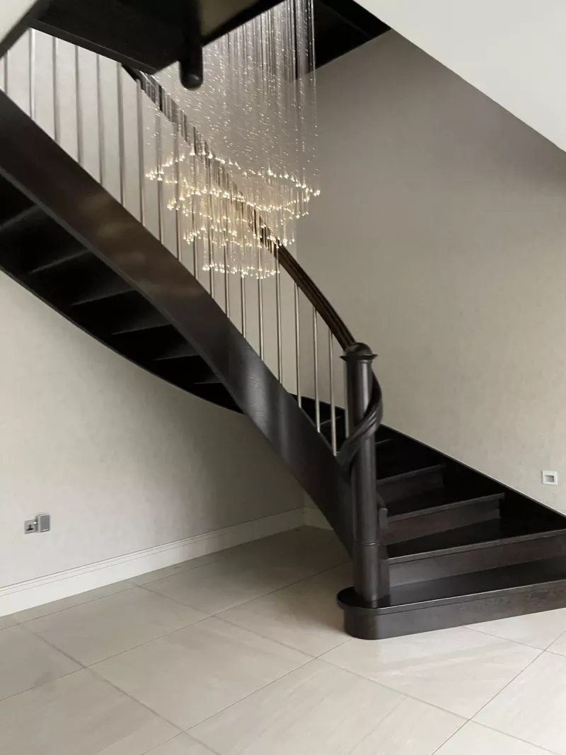 A cascading chandelier lighting the turn of a dark timber staircase