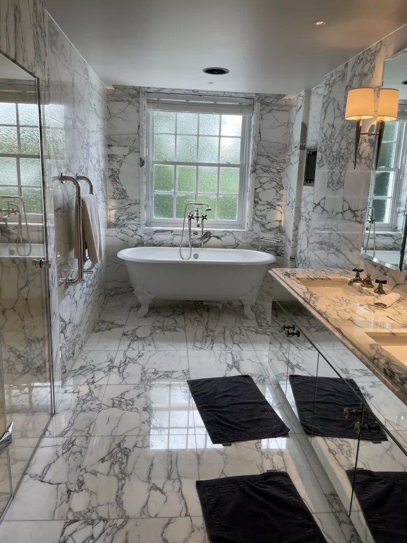 Freestanding bath below the window in a marble lined bathroom