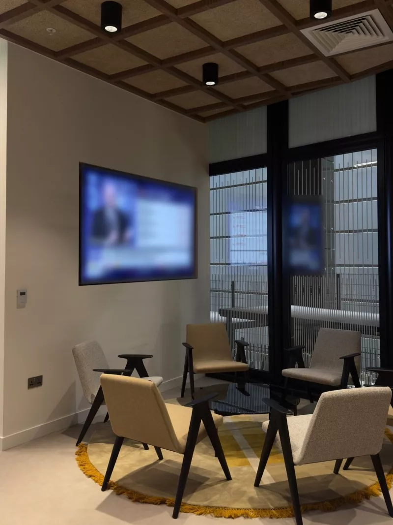 Wall mounted display in an office lounge, with armchairs around a low table