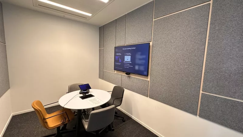 Acoustic panelled meeting room with a wall screen and a touch controller on the round table