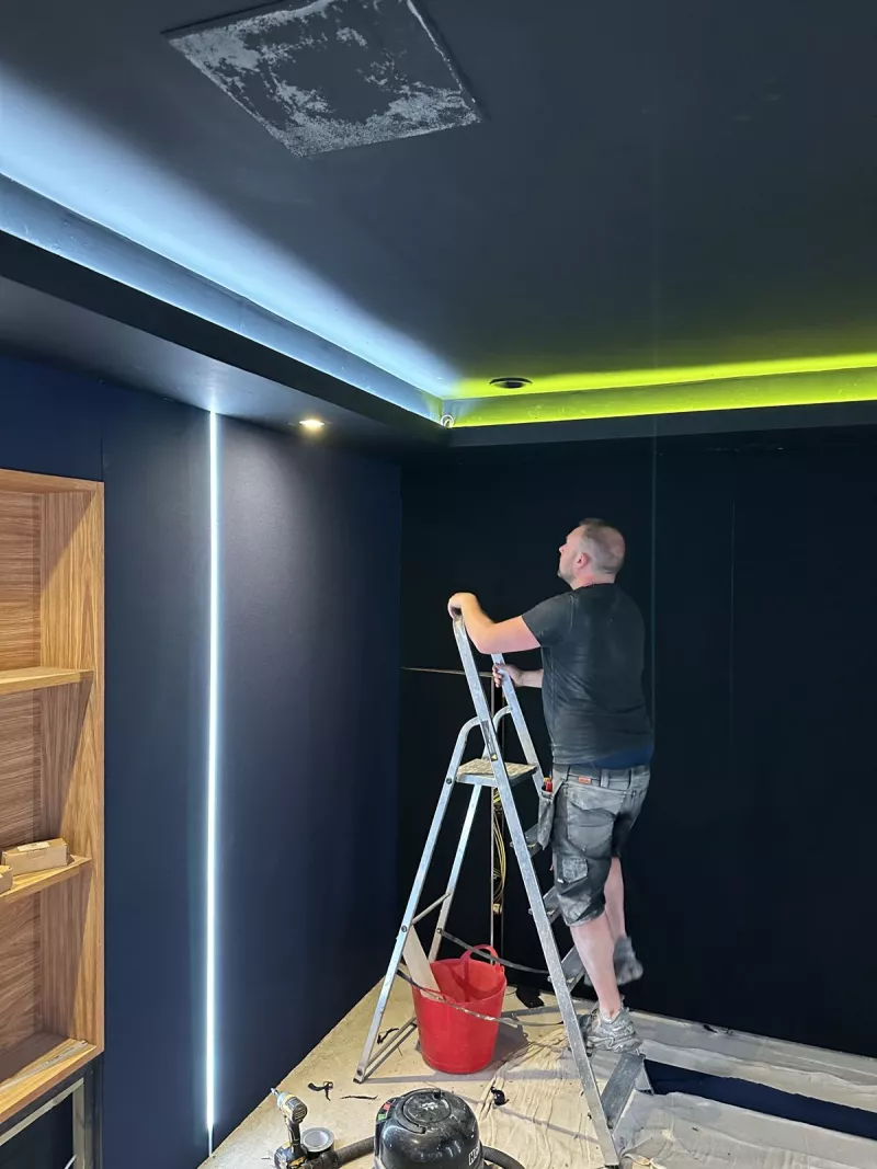 An engineer installing LED strip lighting at the ceiling edge