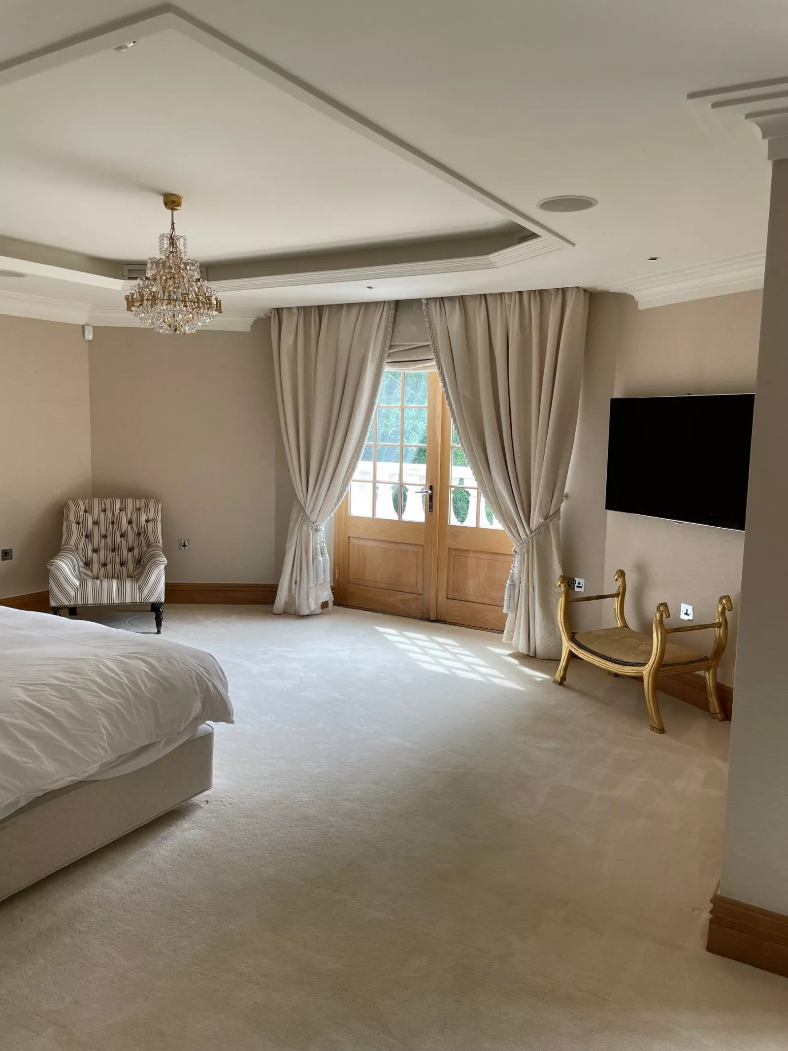 Bedroom with a crystal chandelier, tall curtains and a wall mounted TV, a room a KNX installer in Dublin can set for evening with one press
