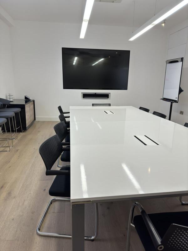 Meeting room wall display with a Sonos soundbar in a recess below it, above a long white table and black chairs in a Dublin office
