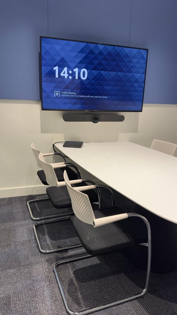 Meeting room video bar installation in Dublin, with a Logitech video bar fixed below a wall display, above a white table and white chairs