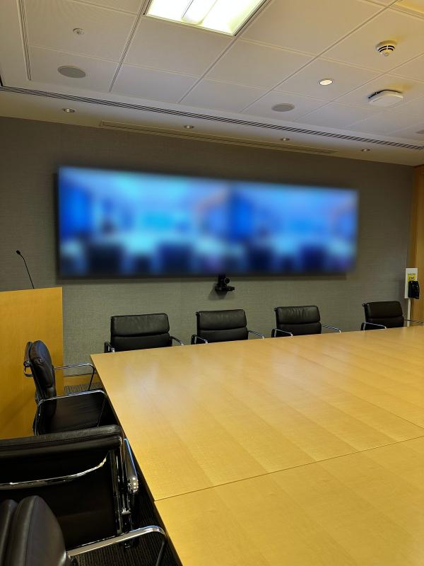 Boardroom video conferencing in Dublin, with twin screens on the end wall, a camera below them and a long timber table with black leather chairs