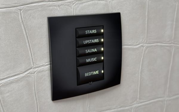 Wall keypad in a Cork house, part of the Control4 to Crestron Home project, with backlit buttons labelled stairs, upstairs, sauna, music and bedtime on a pale crocodile pattern wall
