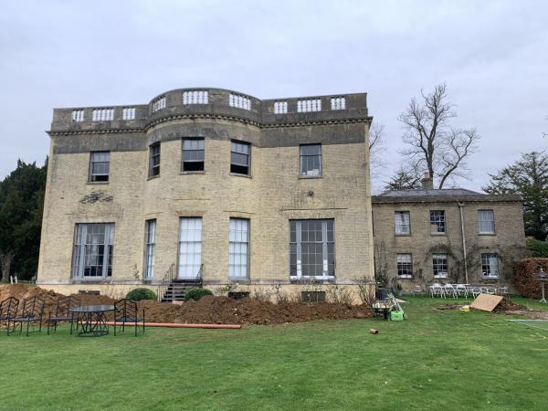 A stone country house with tall sash windows, seen across the lawn