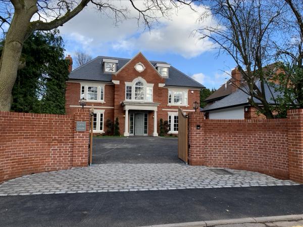 A red brick house with a slate roof behind its entrance gates