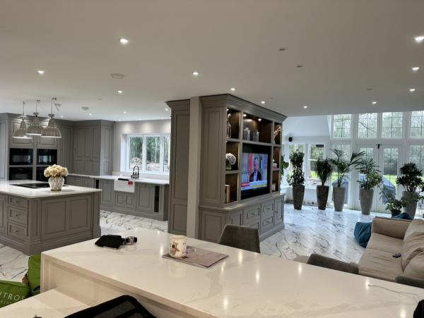 Grey fitted kitchen opening to a sitting area with a television in the shelving