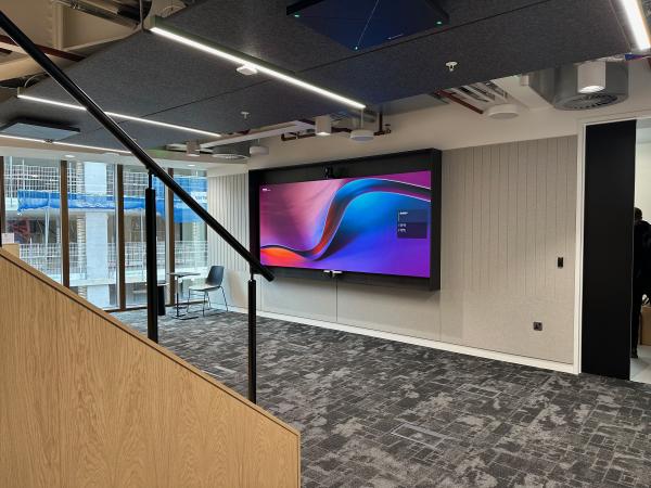 Wall display with a camera above and a video bar below, beside a staircase in an open office