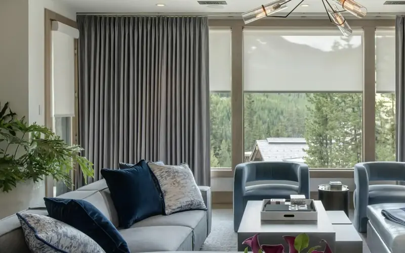Sitting room with grey curtains drawn back at a tall window, with blue armchairs and a pale sofa