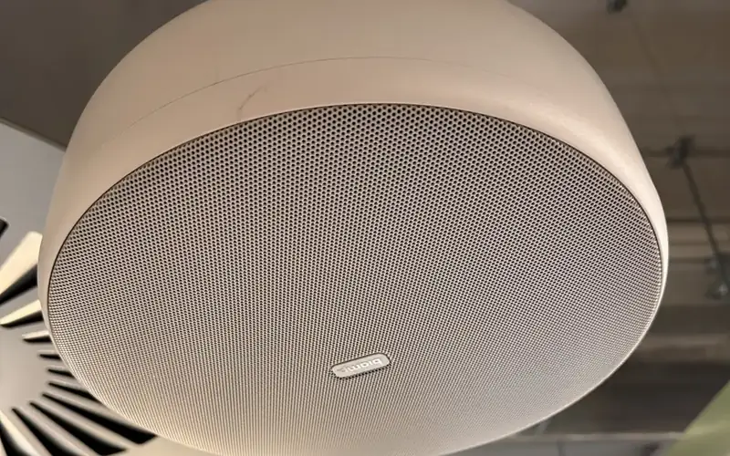 Close up of a white round ceiling audio unit with a mesh grille in a meeting room