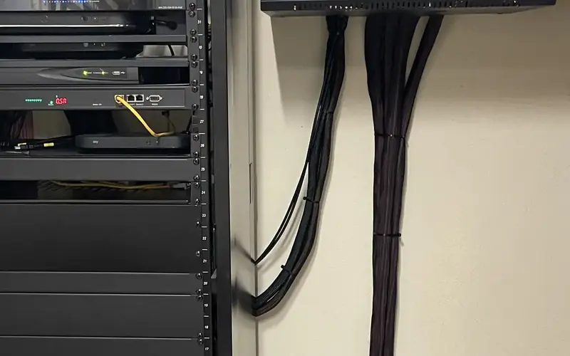 Rack of AV equipment with black cabling clipped in tidy bundles up a pale wall