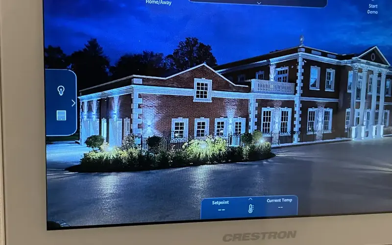Crestron touch panel on a wall with a night time view of a large brick house