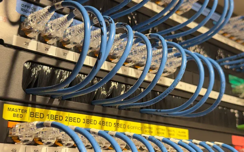 Rows of blue network cables above yellow strips labelled by room
