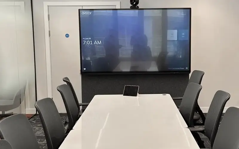 White meeting table with a touch controller in front of a large wall screen