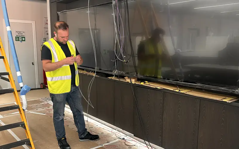 Engineer in a high visibility vest fitting a wall of displays